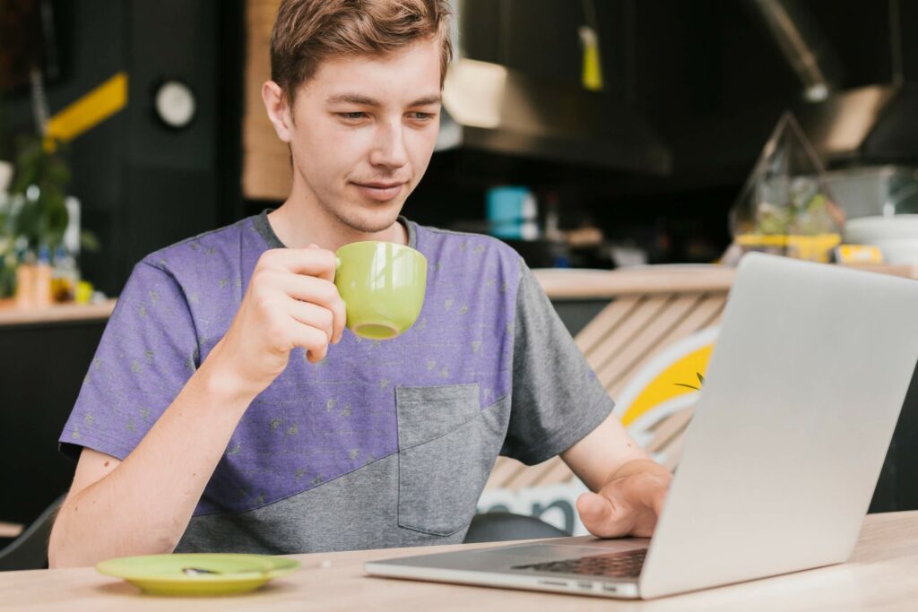 młody człowiek pije kawę przed laptopem