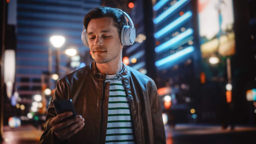 Portret przystojnego mężczyzny w słuchawkach spacerującego nocną ulicą miasta pełną neonów