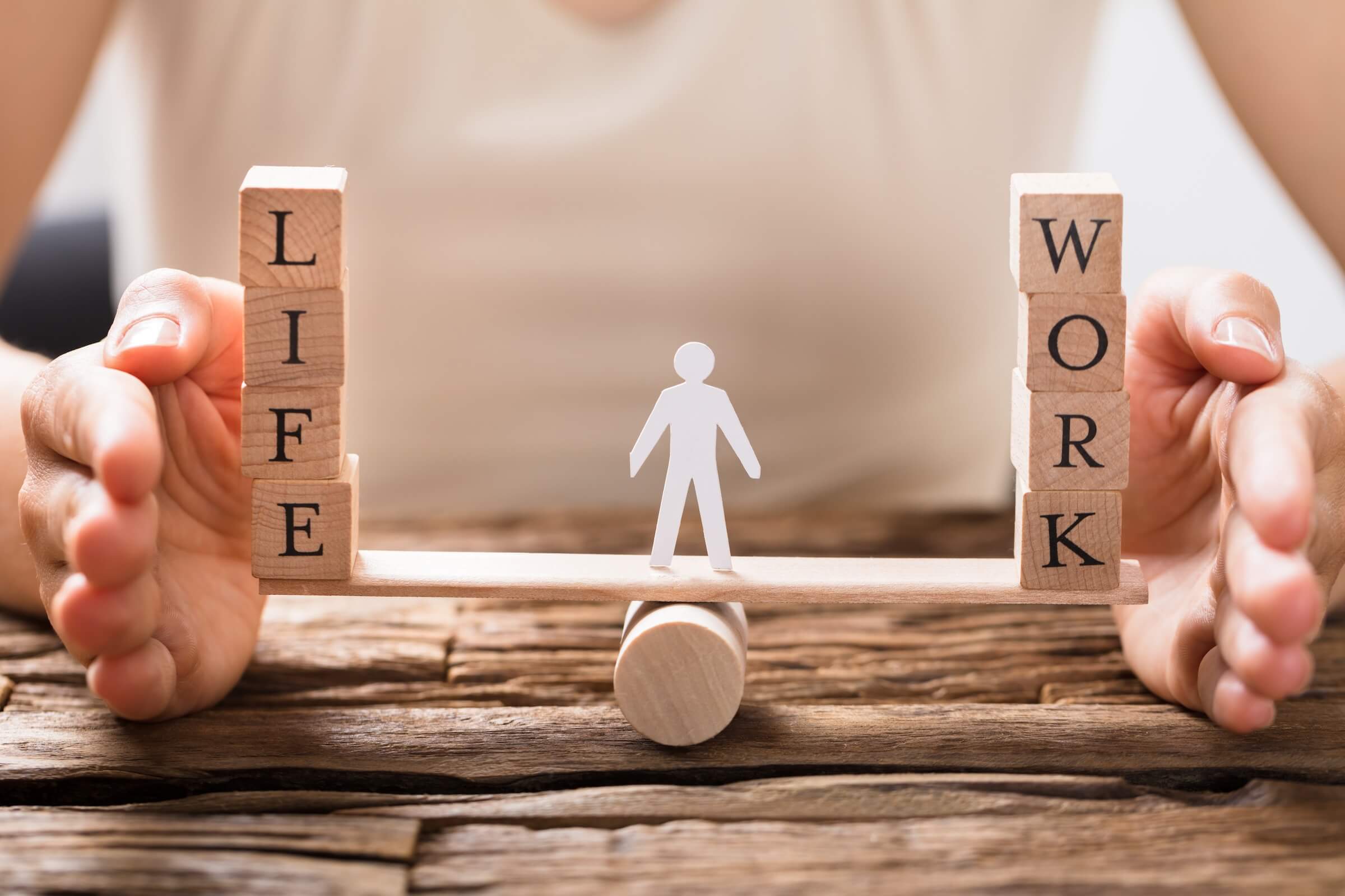 Równoważnia z napisami "LIFE" i "WORK" po obu stronach oraz figurka człowieka w środku, co symbolizuje równowagę między życiem a pracą